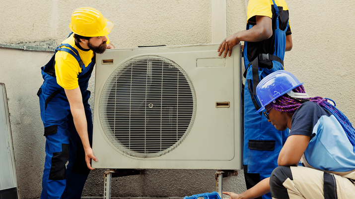 Dos técnicos instaladores certificados realizando la conexión de una unidad exterior de aire acondicionado en una fachada, cumpliendo las normativas de seguridad