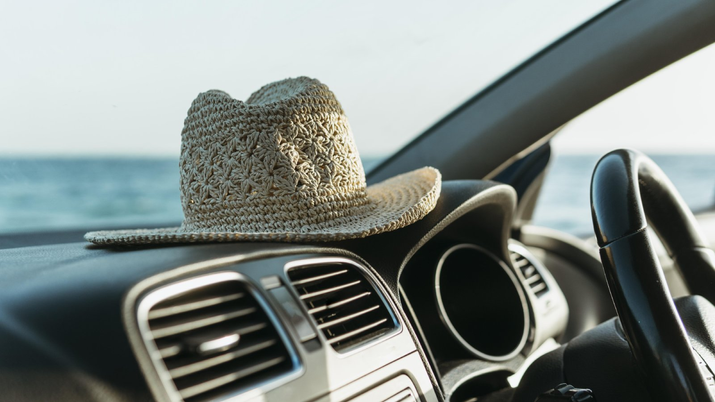 Salpicadero de un coche con un sombrero, ilustrando el concepto de un viaje por carretera en verano con una app de carsharing