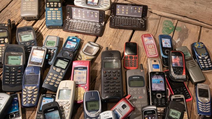 Varios modelos de teléfonos móviles antiguos, incluyendo Nokia y Sony Ericsson, apilados en una caja de cartón, representando la tecnología obsoleta lista para ser reutilizada
