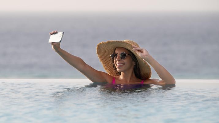 Mujer usando un smartphone cerca de una piscina, ilustrando una situación de riesgo para el dispositivo a pesar de la certificación IP68