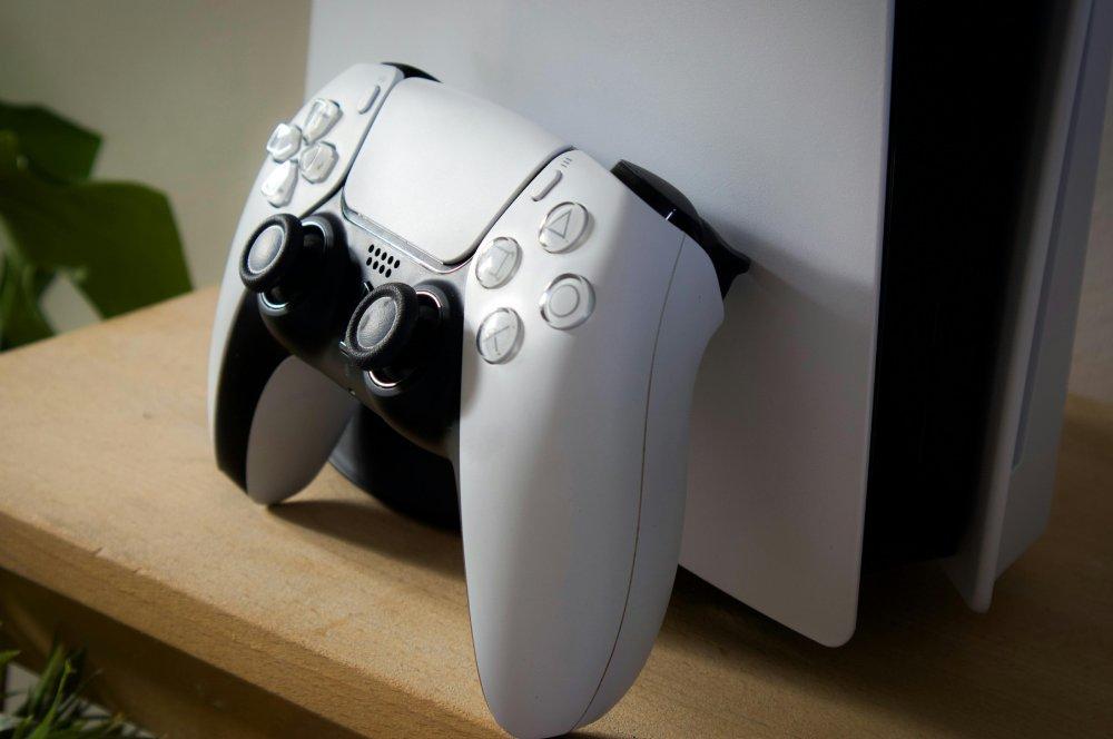 Una imagen de una PS5 con un DualSense apoyado sobre su carcasa