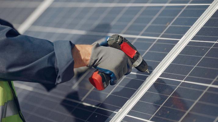 Instalador profesional con equipo de seguridad colocando un panel solar sobre una cubierta de chapa metálica de una casa prefabricada, usando anclajes específicos