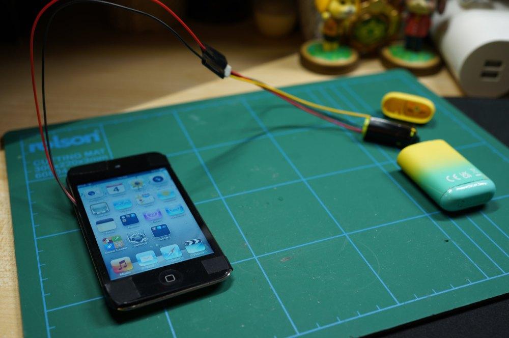 Un iPod Classic blanco conectado mediante un cable USB a la batería de un cigarrillo electrónico, demostrando un método de carga improvisado para dispositivos antiguos