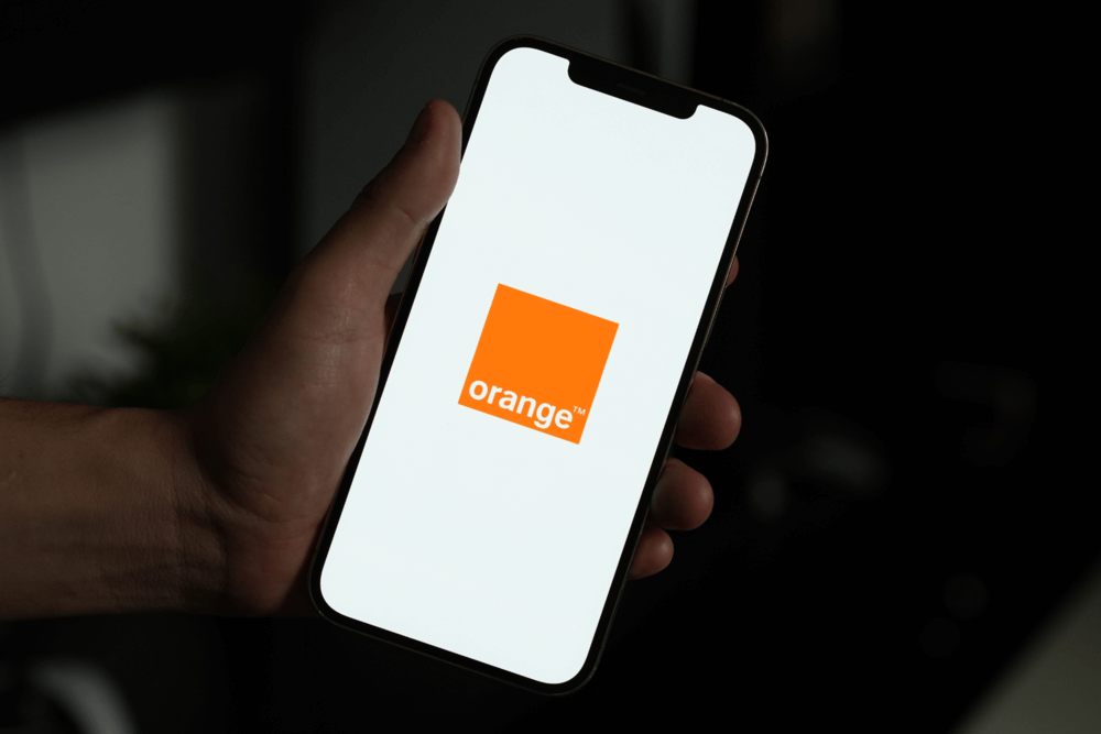 Mano sosteniendo un smartphone con el logotipo de Orange en la pantalla, ilustrando los servicios móviles de MasOrange