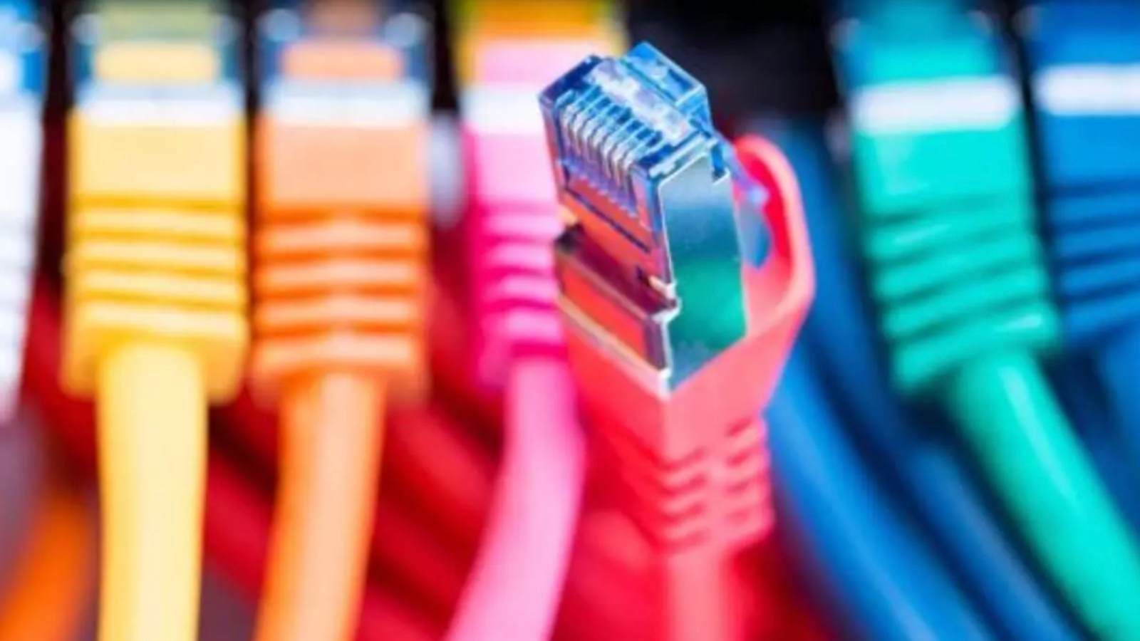 Técnico conectando un cable de red Ethernet azul en un puerto RJ-45 de un switch de red iluminado