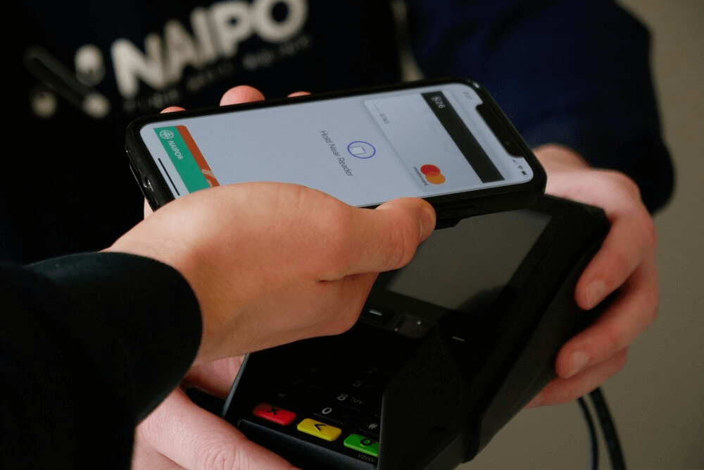 Primer plano de un pago móvil donde un smartphone se acerca a un datáfono para completar una transacción mediante tecnología NFC