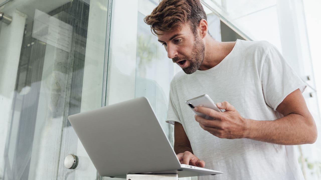 hombre sorprendido con el móvil y PC