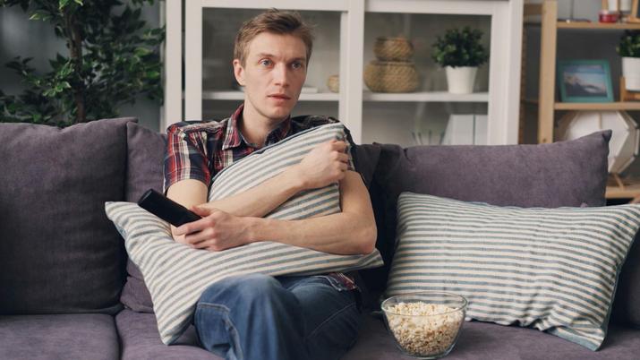 Un chico con cara de incrédulo en el sofá con el mando de la tele